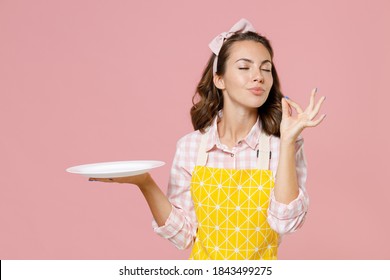 Cute young woman housewife in yellow apron hold empty plate making okay taste delight sign keeping eyes closed doing housework isolated on pastel pink background studio portrait. Housekeeping concept - Shutterstock ID 1843499275