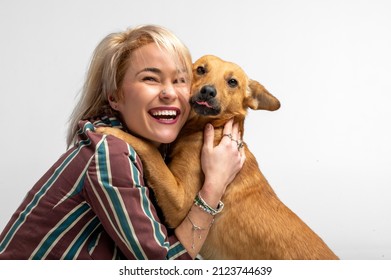 A Cute Young Woman Kisses And Hugs Her Mongrel Dog. Love Between Owner And Dog. Isolated On White Background. Studio Portrait. Girl Huging New Lovely Member Of Family. Pet Care And Animals Concept