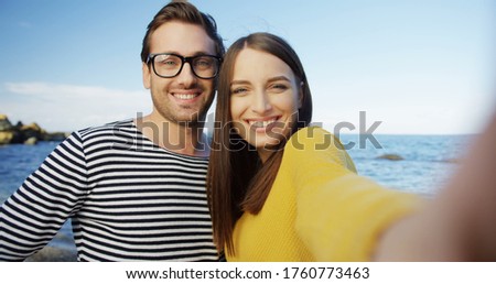 The cute young woman and man taking funny selfies and grimacing on the seacoast. Outdoors. POV. Close up. Portrait shot