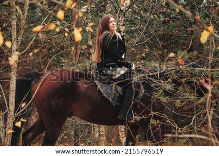Cute young woman on horseback in autumn forest on country road. Rider female drives her horse in Park inclement cloudy weather with rain. Concept of outdoor riding, sports and recreation. Copy space