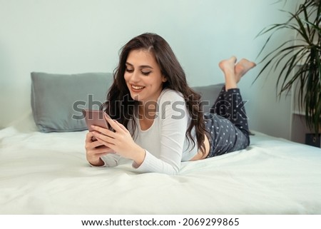 Cute young woman in pajamas using phone on bed. Beautiful woman chating with boyfriend