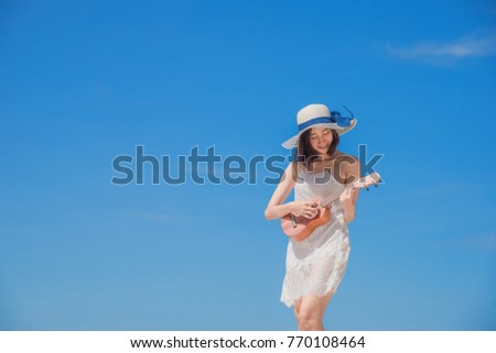 Cute young woman playing akulele on the sea beach with happy smiling on the face at daylight sunny,  cleared blue sky