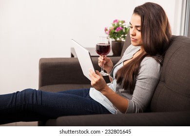 Cute Young Woman Relaxing At Home And Enjoying A Glass Of Wine While Reading