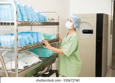 Cute Young Woman In Scrubs Looking At A Cart Full Of Clean And Sterile Clothing In A Hospital