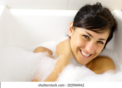 Cute young woman smiling in bath tub full of foam