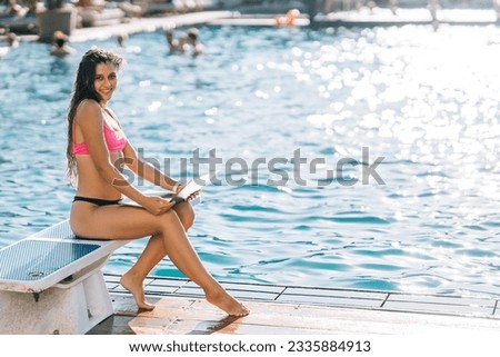Cute young woman in swimsuit sunbathing with a laptop in a pool