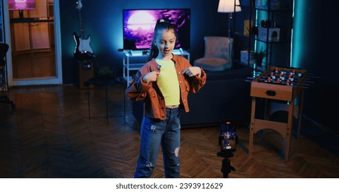 Cute youngster using mobile phone on tripod stabilizer to film dance tutorial for other children watching her online social media content. Girl recording video with smartphone targeting gen Z viewers - Powered by Shutterstock