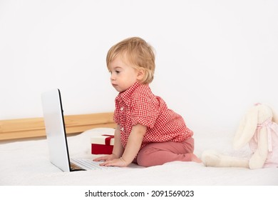 Cute,adorable Blonde Caucasian Baby 1,2 Years Old, Sitting On Bed Modern Light Interior On White Background,look At Laptop,computer.Kid,child,toddler Early Development,online Toy Shopping.Copy Space.