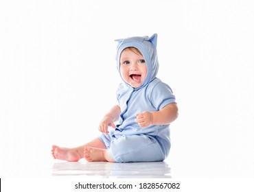 Cutie baby child wearing funny blue suit sitting on floor showing tongue looking at camera. Toddler kid full length portrait. Isolated studio shot on white background with copy space for advertising
