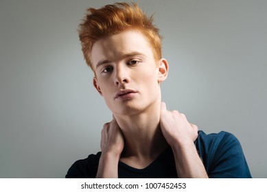 Cutie Pie. Handsome Humourless Red-haired Young Man Wearing A T-shirt And Staring And Touching His Neck