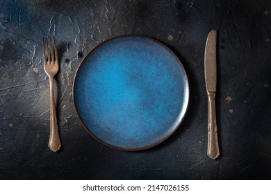 Cutlery With A Blue Plate. A Fork And A Knife On A Vibrant Dish On A Black Slate Background, Overhead Flat Lay Shot