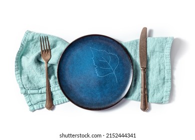 Cutlery With A Blue Plate With A Leaf Design. A Fork, A Knife, And A Dish On A Teal Napkin, Overhead Flat Lay Shot On A White Background