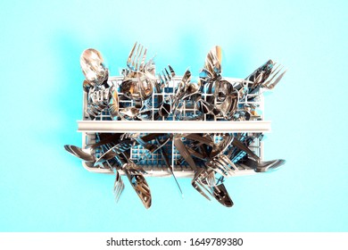 Cutlery In The Dishwasher Basket From Above. Blue Background Image With Space For Text. Clean Spoons, Forks And Knives In A Dishwasher Basket, Close-up. 