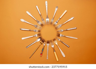 Cutlery. Pop art style. Flat lay of variety of stainless steel, antique silverware and gold forks arranged in circle over orange studio background. History, home, real estate, detail, classic concept