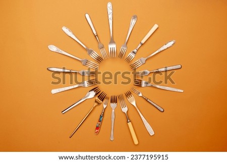 Cutlery. Pop art style. Flat lay of variety of stainless steel, antique silverware and gold forks arranged in circle over orange studio background. History, home, real estate, detail, classic concept