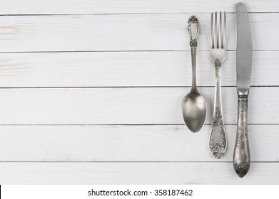 Cutlery set: vintage knife, fork and spoon on white wooden background.