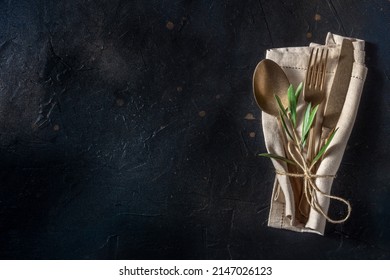 Cutlery. A spoon, a fork, and a knife in a napkin, with an olive branch, on a black background. Modern silverware on a dark table with copy space, overhead flat lay shot