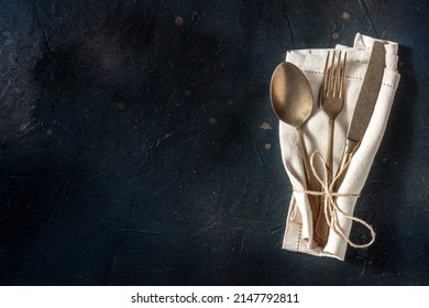 Cutlery. A spoon, a fork, and a knife in a napkin on a black background. Modern silverware on a dark table with copy space, overhead flat lay shot
