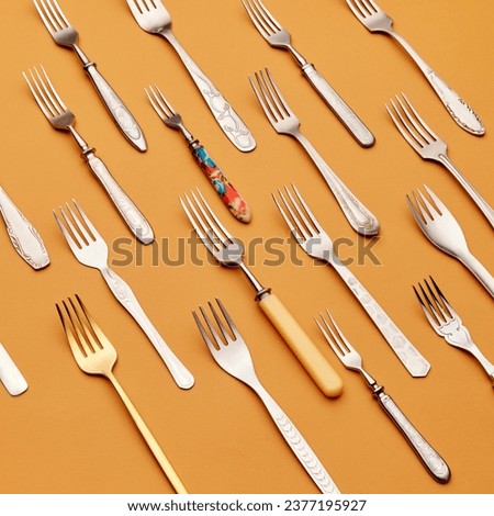 Cutlery. Top view of variety of stainless steel, silver and golden forks symmetrically arranged against orange studio background. Concept of kitchen, vintage, retro, holiday, table setting
