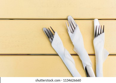 Cutlery Wrapped In A Paper Napkin On A Yellow Wooden Background.