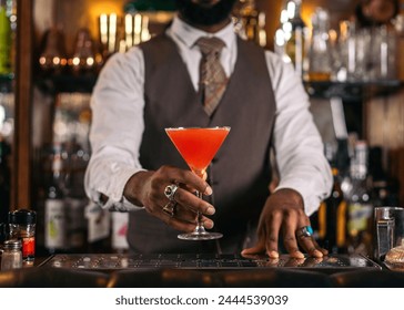 Cutout of a black bartender offering a cocktail served in a martini glass in a traditional cocktail bar - Powered by Shutterstock