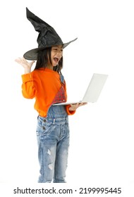 Cutout Isolated Studio Shot Of Asian Young Cute Girl In Casual Orange Party Costume With Black Witch Hat Standing Holding Hand Up Say Hi Greeting On Video Call Via Laptop Computer On White Background.