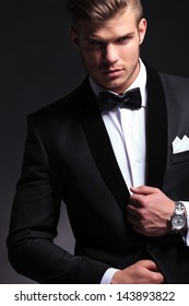 cutout picture of an elegant young fashion man fixing his tuxedo while looking at the camera.on black background