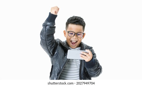 Cutout Portrait Of Lively Young Asian Boy On Casual Black Jacket Looking At Mobile Phone And Happily Shouting Out And Raising Hand Up As Mission Completed, Task Accomplished And Win Online Game Play