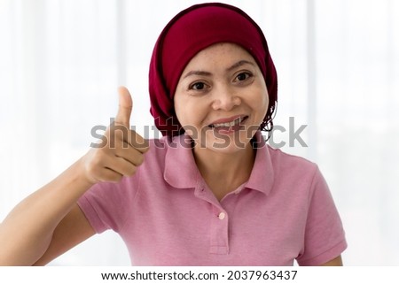 Cutout portrait of lovely Asian woman as breast cancer patient on pink shirt, cover head by red scarf, happily thumb up with smile as safe sign and great motivation to survive from disease treatment