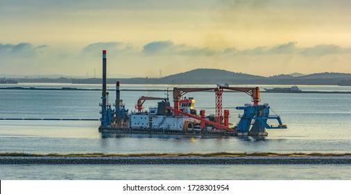 Cutter Suction Dredger At Work Of Land Reclamation For New Ports Positioned On Spuds As Anchors And Discharge Dredged Soil Through A Floating Pipeline. Singapore, Southeast Asia.