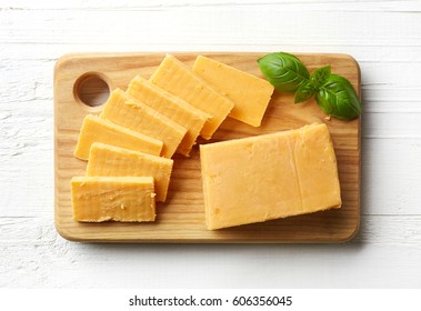 Cutting Board Of Cheddar Cheese On White Wooden Background. From Top View