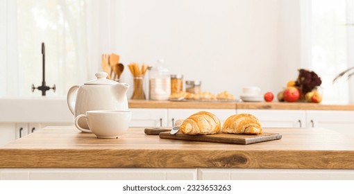 Cutting board with croissants, knife, teapot and cup on wooden table top in modern kitchen - Shutterstock ID 2323653263