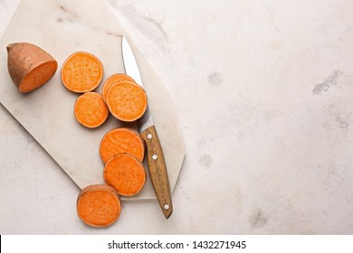 Cutting board and knife with raw sweet potato on light background