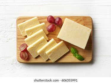 Cutting Board Of White Cheddar Cheese On White Wooden Background. From Top View