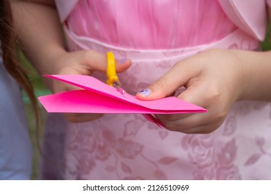 Cutting From Colored Paper. Details Of Master Class. Children's Creativity. Needlework Lesson. Child Cuts Pink Paper With Scissors. Making Origami.