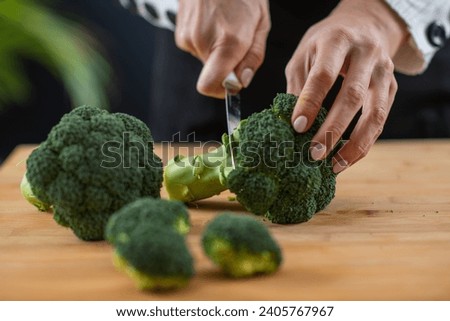 Cutting fresh organic broccoli, a superfood rich in vitamin K, vitamin C, folic acid, potassium, phytonutrients, and fibers.