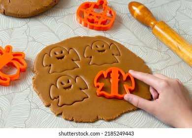 Cutting Halloween gingerbread in shape of ghosts from dark honey dough with spices. Dough, rolling pin and Halloween cookie cutter on table