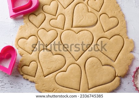 Cutting heart shaped cookies with cookie cutters on a light blue tabletop, top view. Stage of cooking delicious homemade pastry.