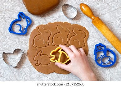 Cutting out Easter gingerbread in shape Easter bunnies from dark honey dough with spices. Dough, rolling pin and different Easter cookie cutters on table