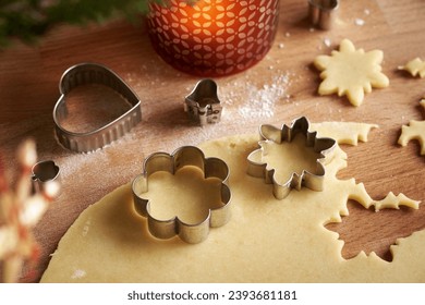 Cutting out flower and star shapes from pastry dough to prepare Linzer Christmas cookies, close up