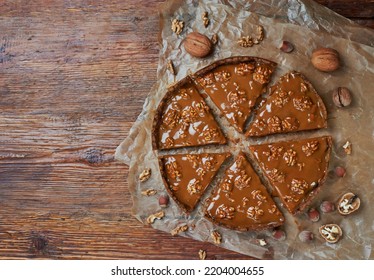 Cutting Piet With Caramel And Walnut On Baking Paper On Wooden Table. Brown Wooden Background. Top View