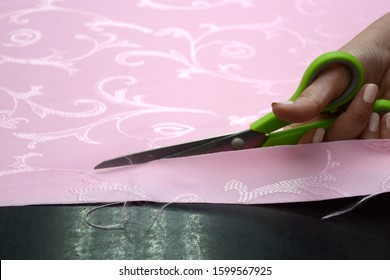 Cutting pink fabric in a sewing workshop on a black table. Preparing for sewing curtains. Cutting with light green tailor scissors. Small business. - Powered by Shutterstock