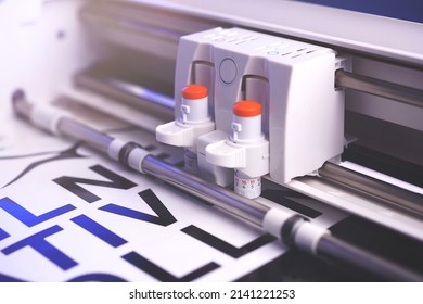 cutting plotter machine with adjustable blades makes adhesive lettering from black vinyl foil in bright light with blue highlights. selective focus. advertising concept