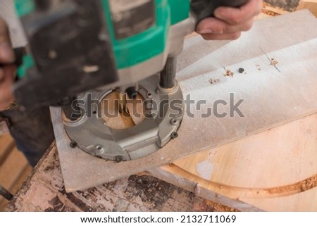 Cutting a round shape from a thick slab of wood. Using a plunge wood router with a circle cutting jig. Making the head of a bar stool at a workshop.