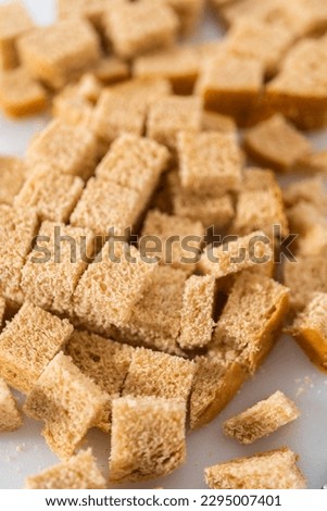 Cutting stale bread with a bread knife on a white cutting board to make croutons.