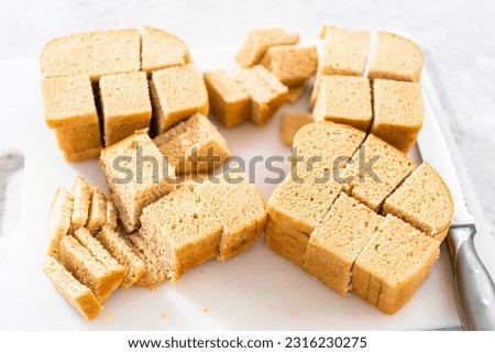 Cutting stale bread with a bread knife on a white cutting board to make bread pudding.