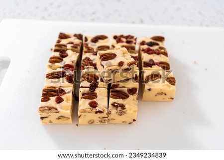 Cutting white chocolate cranberry pecan fudge into small pieces on a white cutting board.