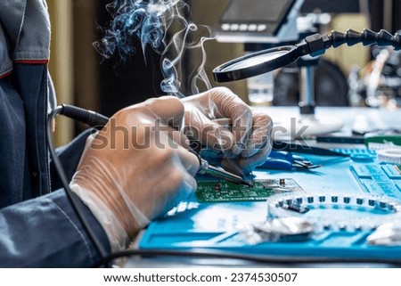 Cutting-edge electronics workshop scene showcases a skilled technician's hands meticulously soldering on a modern circuit board. Smoke rises, tech-focused emphasizing precision and high-tech expertise