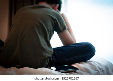 Cyber bullying concept. Back oa a young asian tween / teenage boy sit cross legged alone in bedroom, plug finger in ears feeling stressed, frustrated, overwhelmed with online bullying in social media.