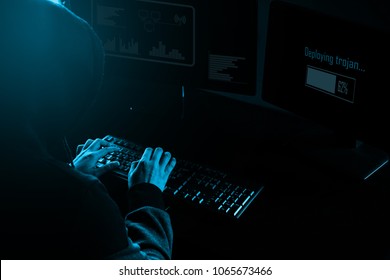 Cyber crime concept. A hooded hacker working in front of his computer deploying trojan virus.